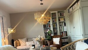 A cozy living room with a round coffee table, two armchairs, a sofa, a bookshelf, and a decorative chandelier. - Hotel a Licorne (Carnac)