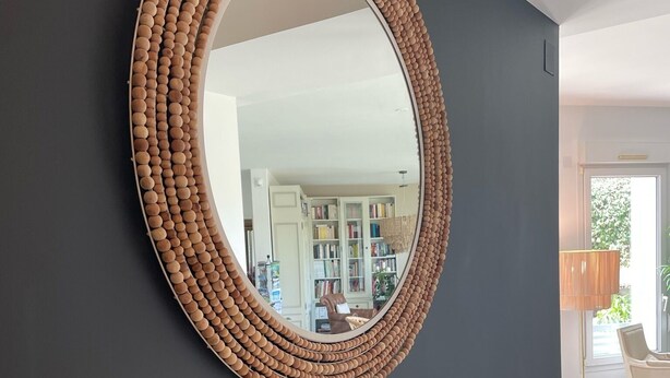 A round mirror with a textured frame on a dark wall. Below the mirror, there is a glass console with a clear lamp and a decorative vase. - Hotel a Licorne (Carnac)