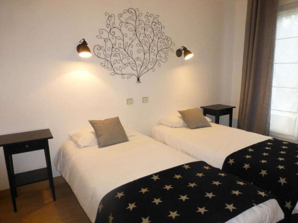 Une chambre avec deux lits, chacun étant équipé d’un oreiller et d’une table de chevet. Un élément décoratif orne le mur au-dessus des lits, et deux lampes sont fixées au mur.