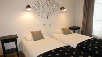Une chambre avec deux lits, chacun étant équipé d’un oreiller et d’une table de chevet. Un élément décoratif orne le mur au-dessus des lits, et deux lampes sont fixées au mur.