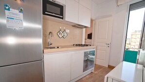 Una cocina compacta con refrigerador de acero inoxidable, microondas, estufa a gas y horno empotrado. Hay un tapete pequeño en el suelo y una ventana con vista al exterior.