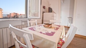 Un comedor con una mesa dispuesta para cuatro personas, un radiador y vistas a edificios a través de una ventana.