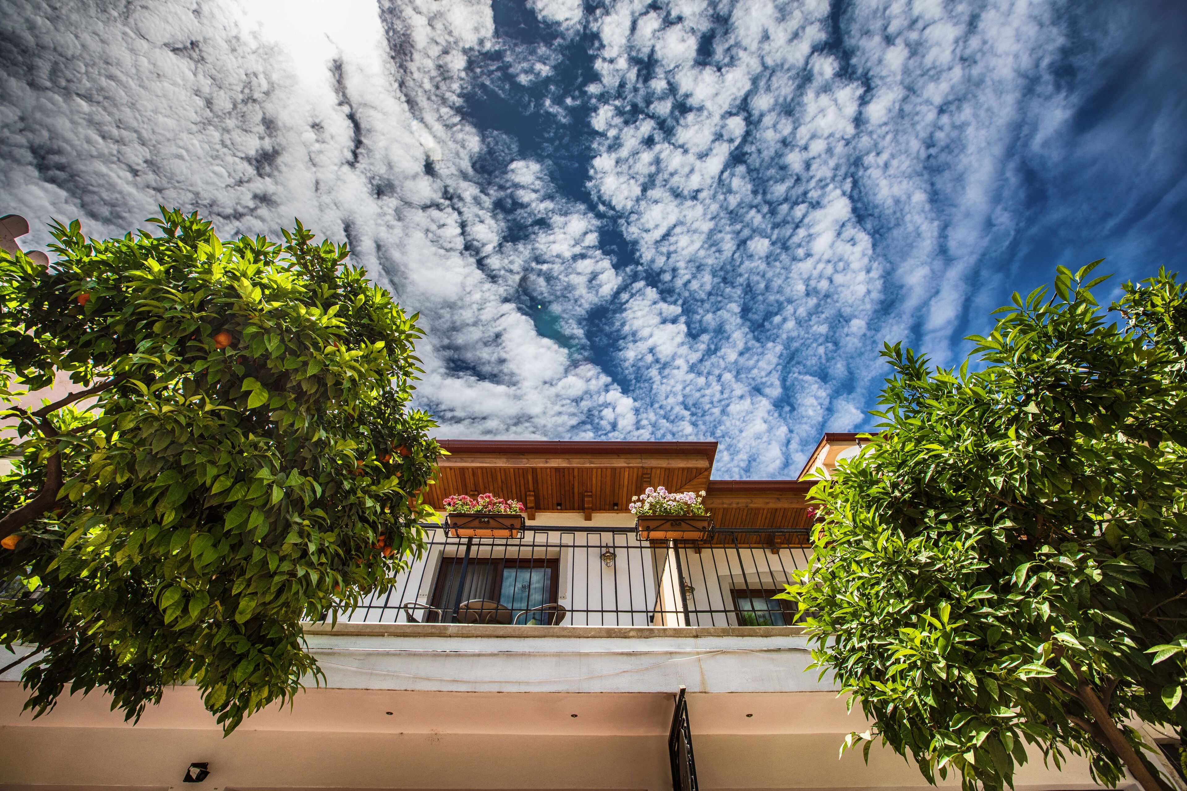 Un edificio con balcón, cielo despejado con nubes y árboles verdes al frente.