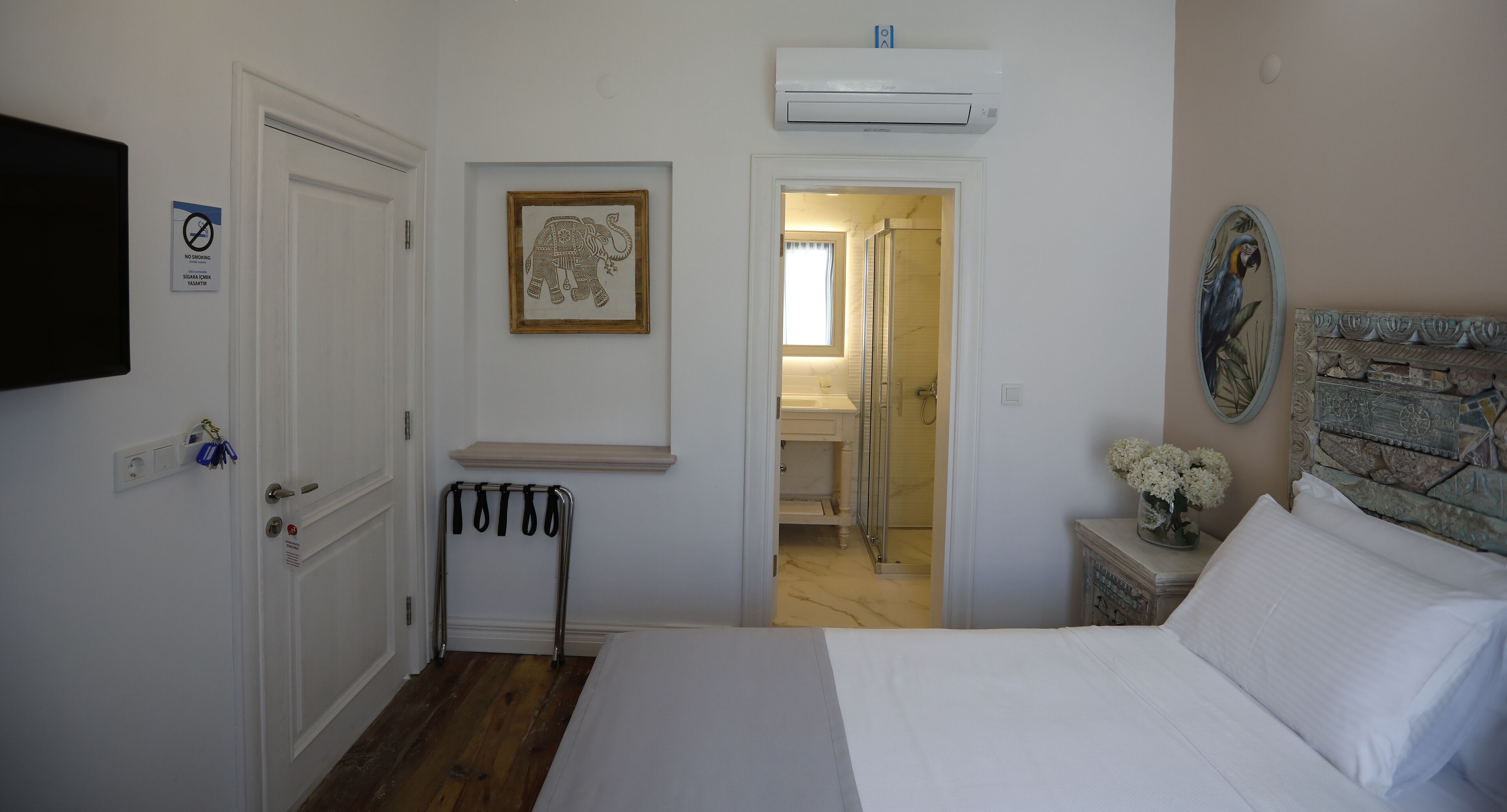 A hotel room with a bed, a shower, a sink, and a framed elephant picture.