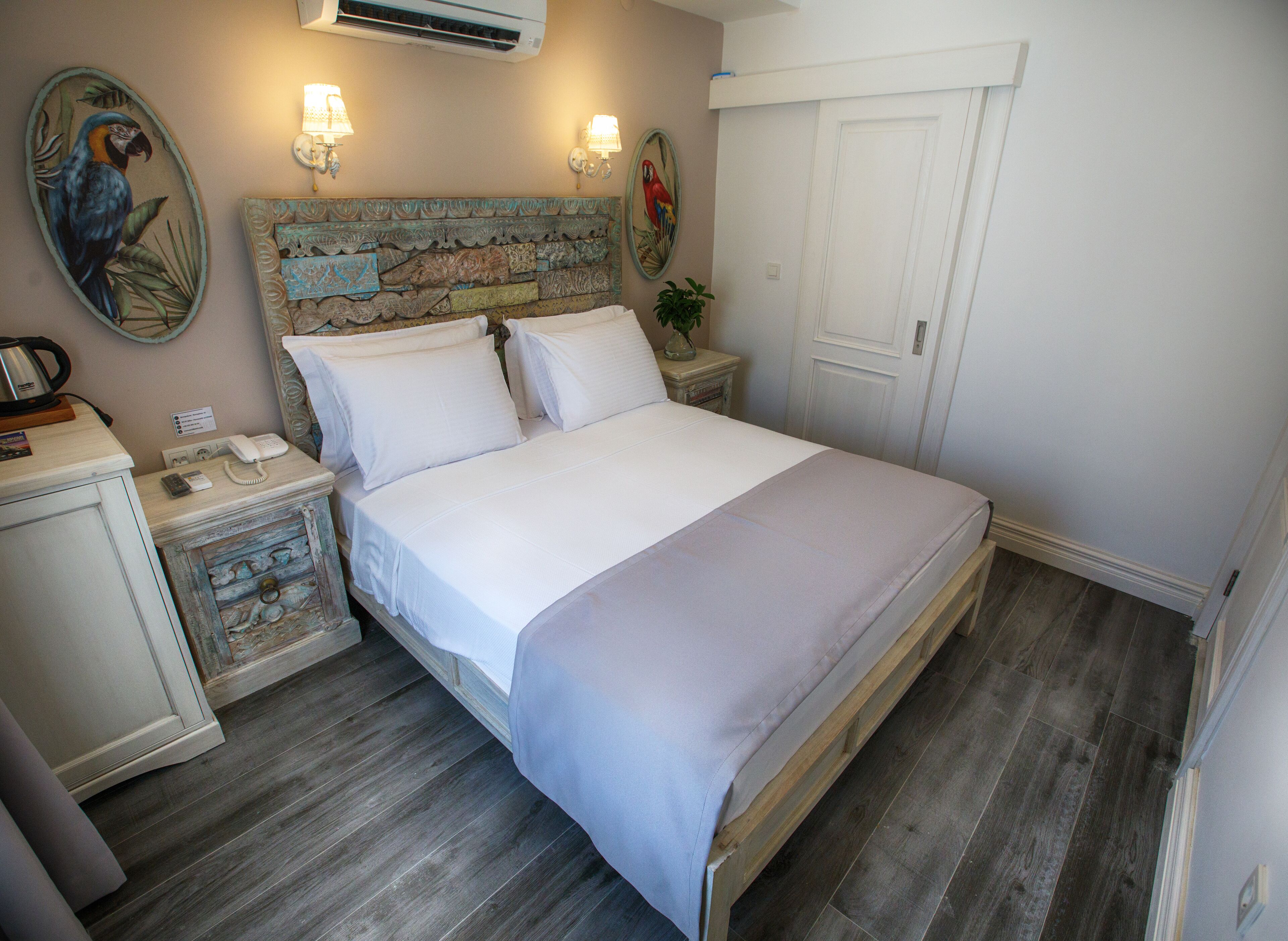 Een slaapkamer met een houten bed, witte lakens, een nachtkastje met een lamp, een telefoon en een decoratief hoofdeinde.