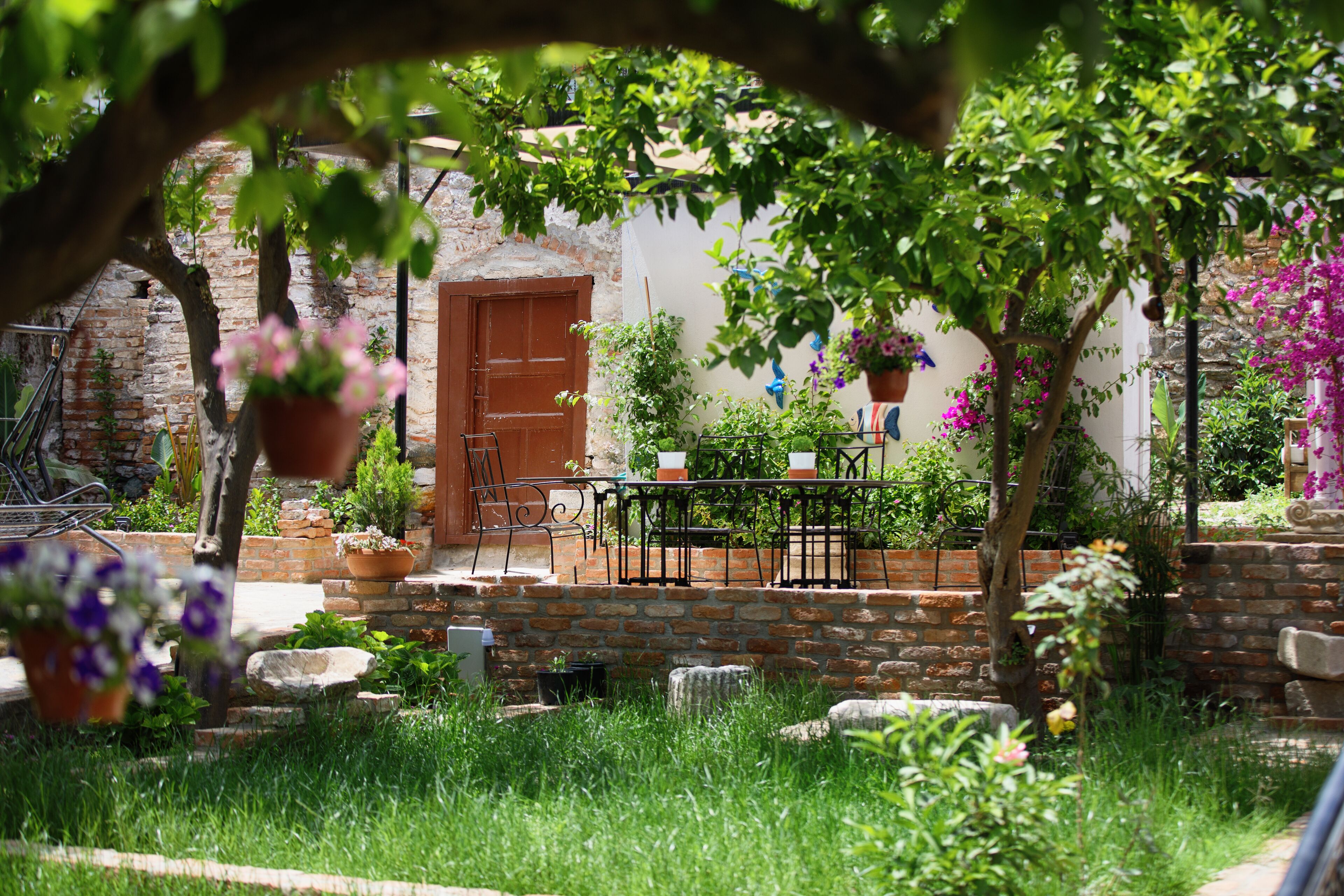 A rustic courtyard with a brick wall, a wooden door, and a metal table with chairs.