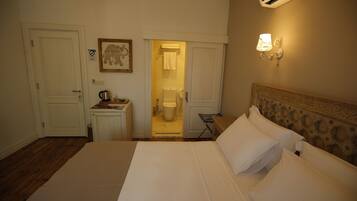 Habitación de hotel con cama, escritorio con hervidor, un cuadro en la pared y equipo de aire acondicionado.