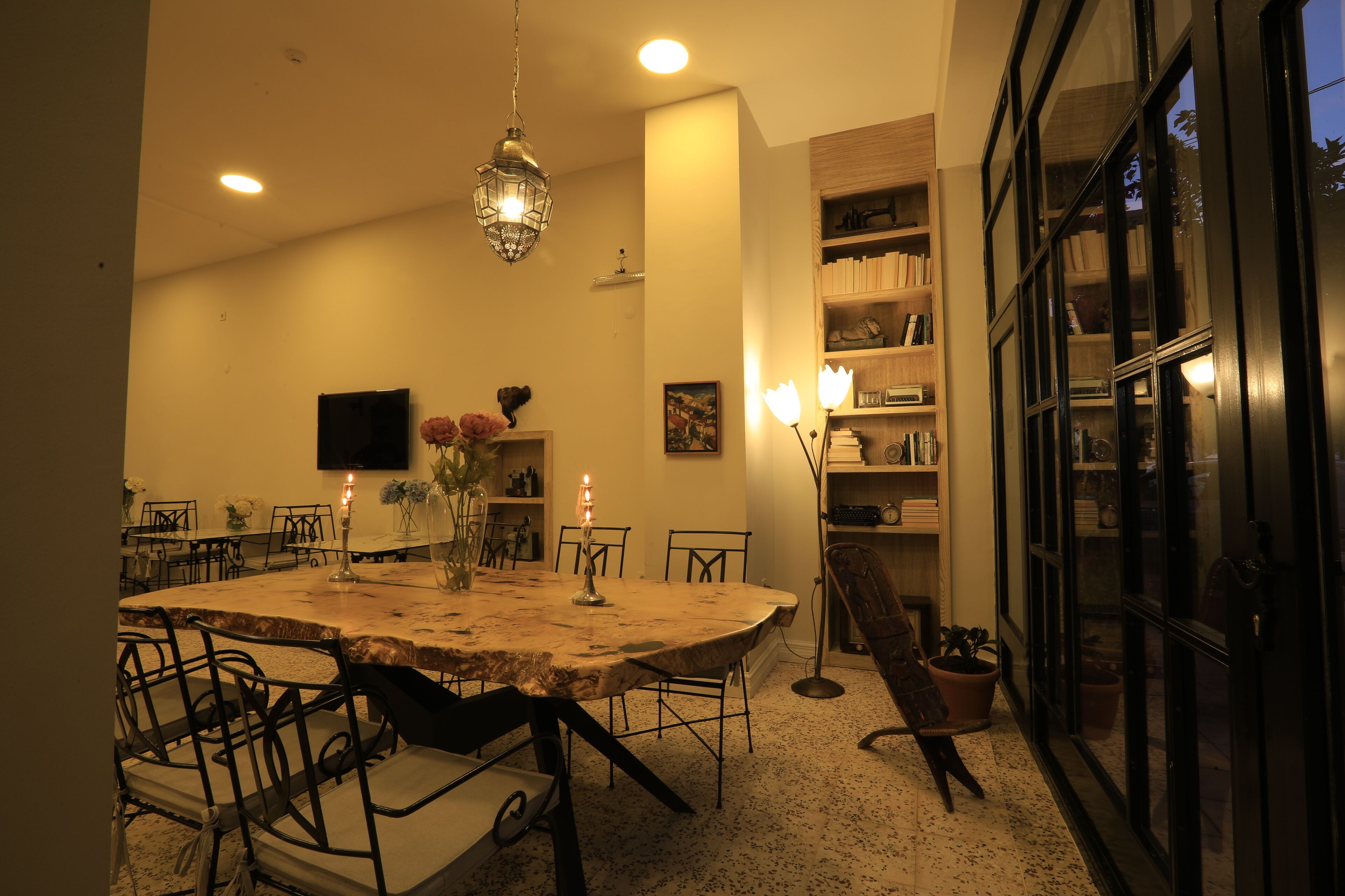 Uma sala de jantar com mesa redonda, cadeiras, um lustre e uma estante de livros.