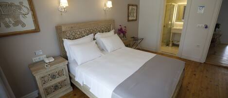 Una cama bien hecha con ropa de cama blanca, una mesita de noche de madera con una lámpara y un cuadro con una representación de un elefante en la pared.