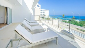 A rooftop terrace with white lounge chairs and a clear view of the ocean and a hotel building in the background. - Protaras holiday villa - rentprivatevillas 100 (Protaras)