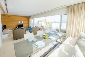 A modern hotel room with a dining area, a sofa set, and a large window offering a view of the sea. - Protaras holiday villa - rentprivatevillas 100 (Protaras)