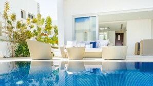 A modern pool area with clear blue water, white lounge chairs, and a glass door leading to a room. - Protaras holiday villa - rentprivatevillas 100 (Protaras)