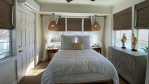 Une chambre à coucher comprenant un lit, un ventilateur de plafond, une fenêtre avec des rideaux, une table de chevet et une commode.