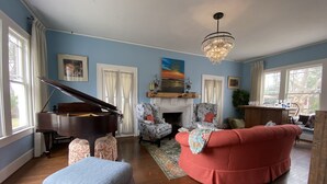 Un salon avec un grand piano, un canapé rouge, des fauteuils à motifs et un lustre.