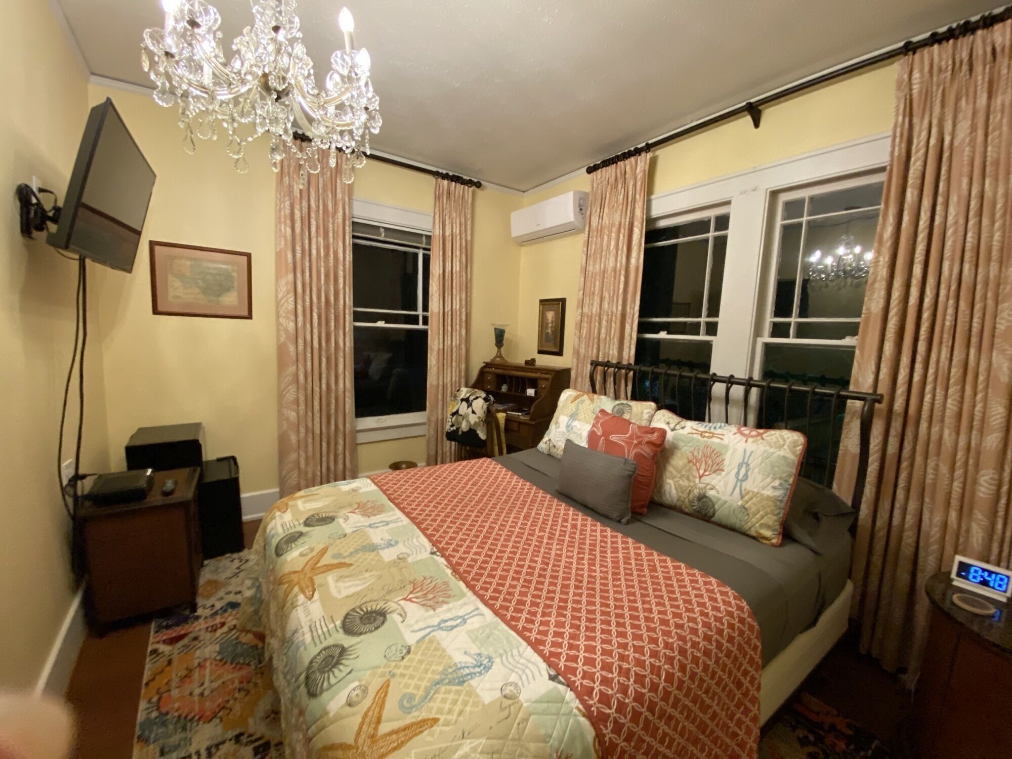 A bedroom with a bed, a chandelier, a desk, and a window with curtains.