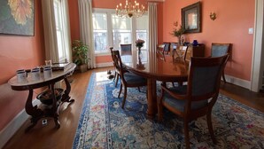 Une salle à manger avec une grande table en bois, six chaises, un lustre et un tapis à motifs.
