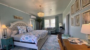 A bedroom with a bed, bedside tables, a desk, a chandelier, and a window with curtains.