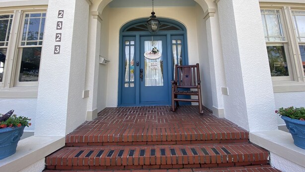 A building entrance with a blue door, a wooden chair, and a brick staircase.