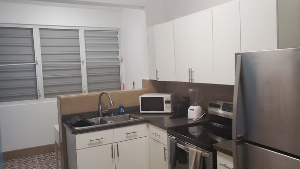 Una cuina compacta amb armaris blancs, nevera d'acer inoxidable, microones, fogó i un rentaplat.