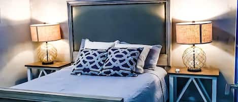 Un dormitorio con una cama, dos mesitas de noche, un aire acondicionado instalado en la pared y un cuadro con pájaros coloridos.