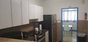 A compact kitchen with white cabinets, a black refrigerator, a coffee maker, and a blender on the counter.