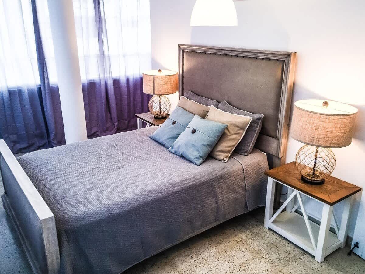 A bed with a headboard, two bedside tables with lamps, and a window with curtains.