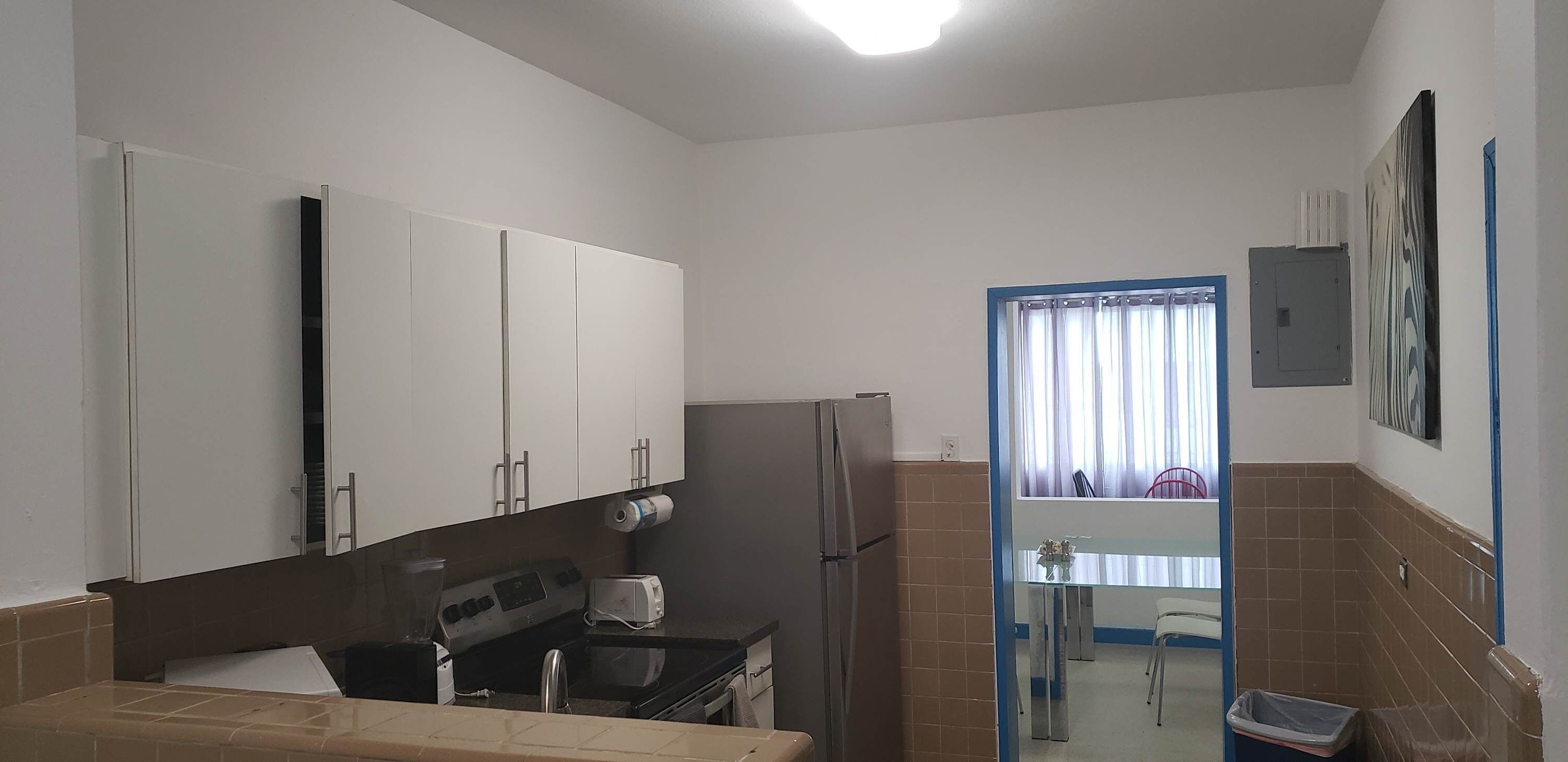 Una cocina compacta con armarios blancos, un refrigerador, una estufa y un lavamanos.