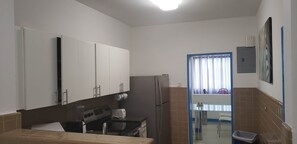 Une cuisine de taille réduite avec des meubles blancs, un réfrigérateur, une cuisinière et un évier.