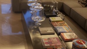 Un salon comprenant un canapé, une table basse avec des livres et des objets décoratifs, et une vue sur des immeubles par une fenêtre.