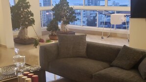 Un salon moderne avec un canapé gris, une table basse en bois et de grandes fenêtres donnant sur la ville.