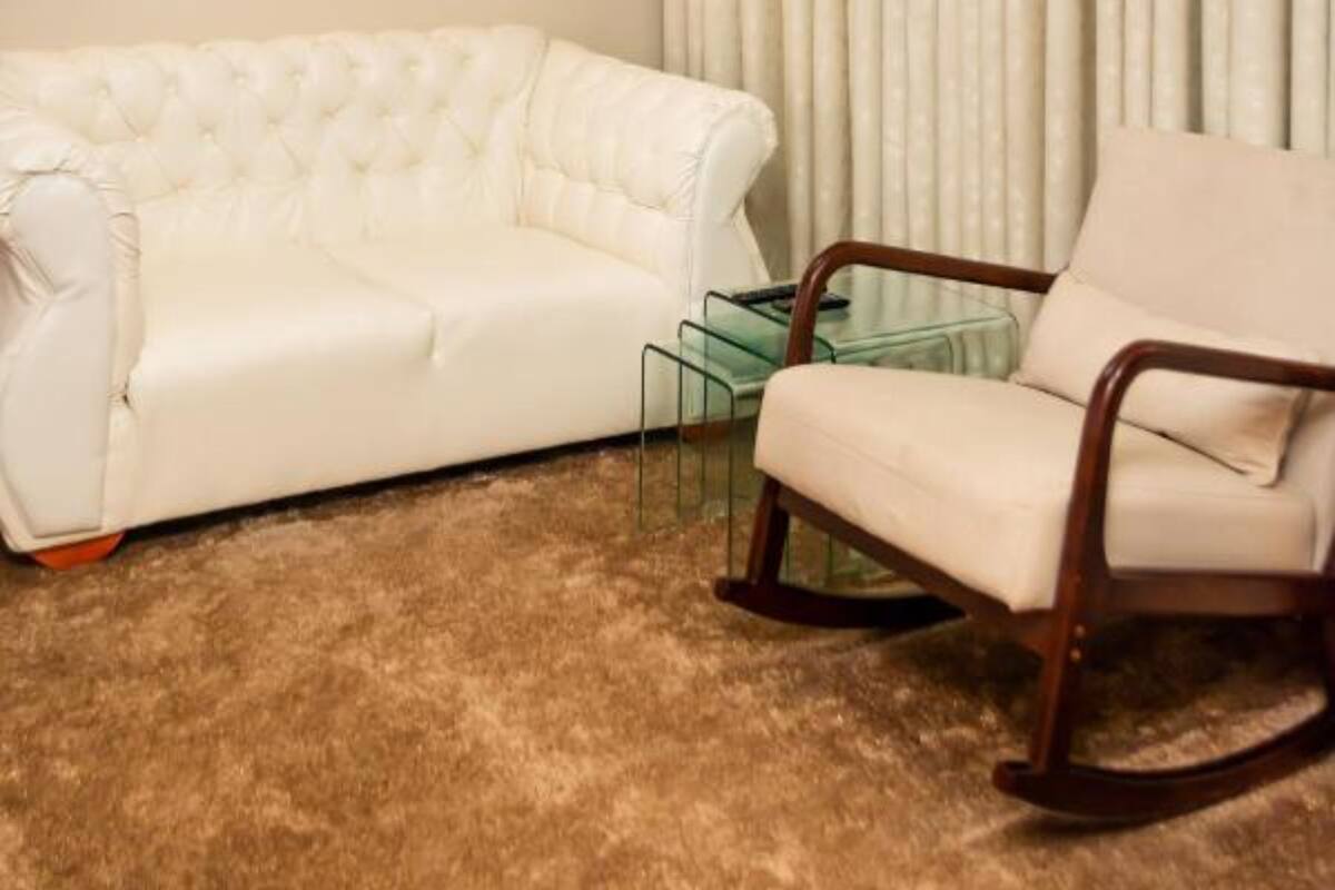 Un salon avec un canapé blanc, un fauteuil à bascule en bois, une table basse en verre et un rideau.