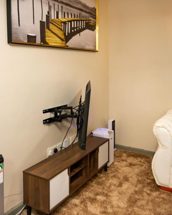 A room with a TV mounted on a wooden stand, a white chair, and a painting on the wall.