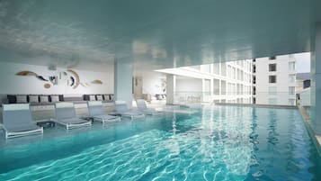 An indoor swimming pool with lounge chairs, a modern ceiling design, and a white building in the background.