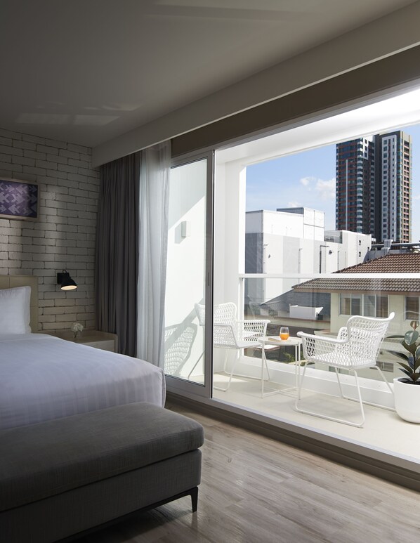Une chambre d’hôtel moderne avec un grand lit, un balcon doté de chaises blanches et une vue sur la ville.