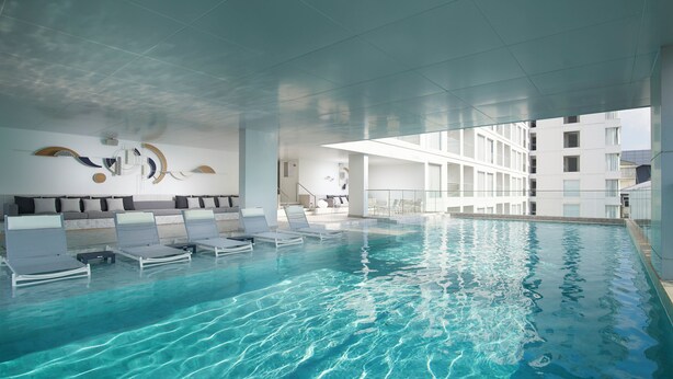 Een binnenzwembad met helder water, ligbedden en een modern interieur.
