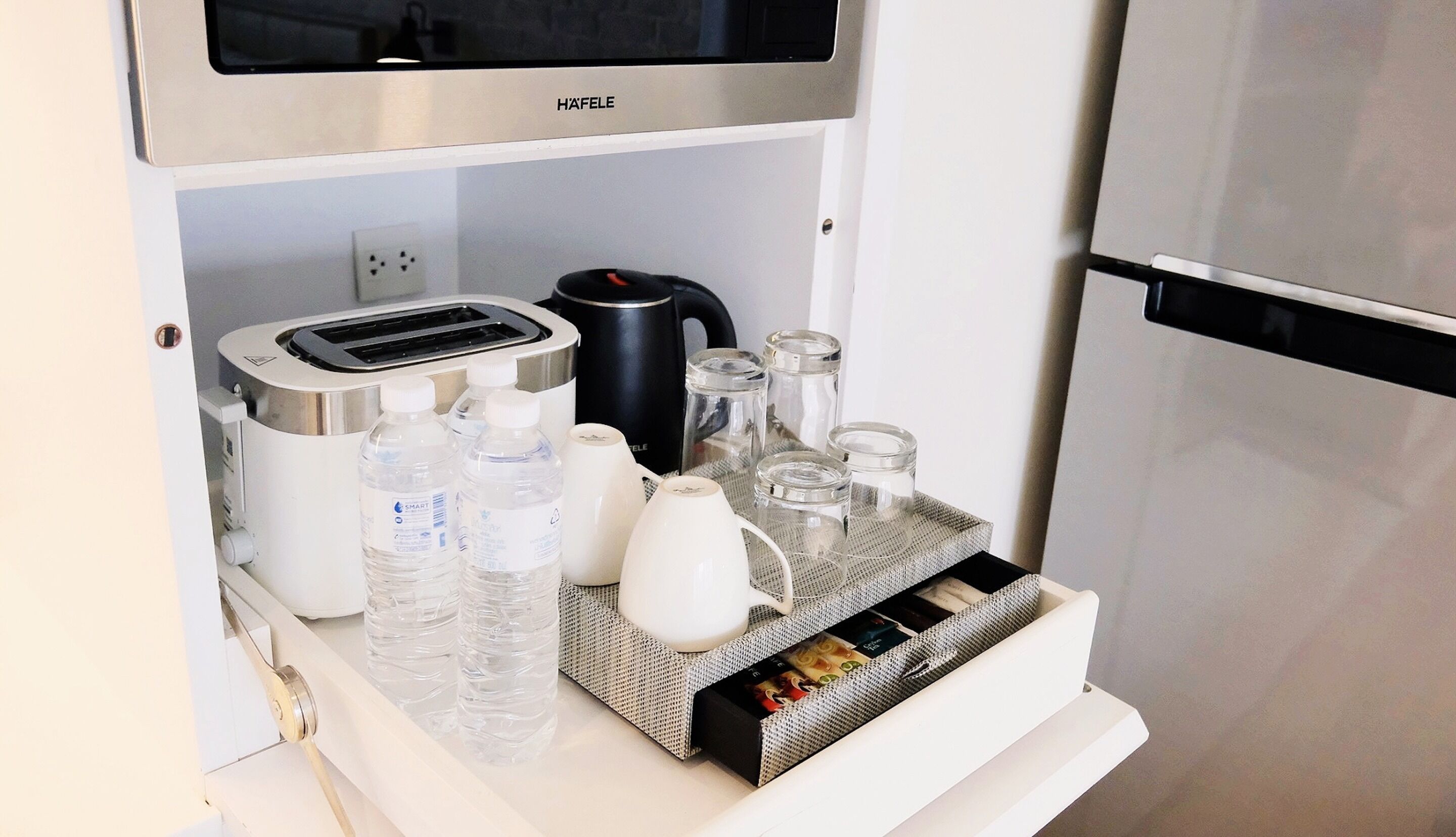 A minibar with a coffee maker, water bottles, a kettle, and a small refrigerator.