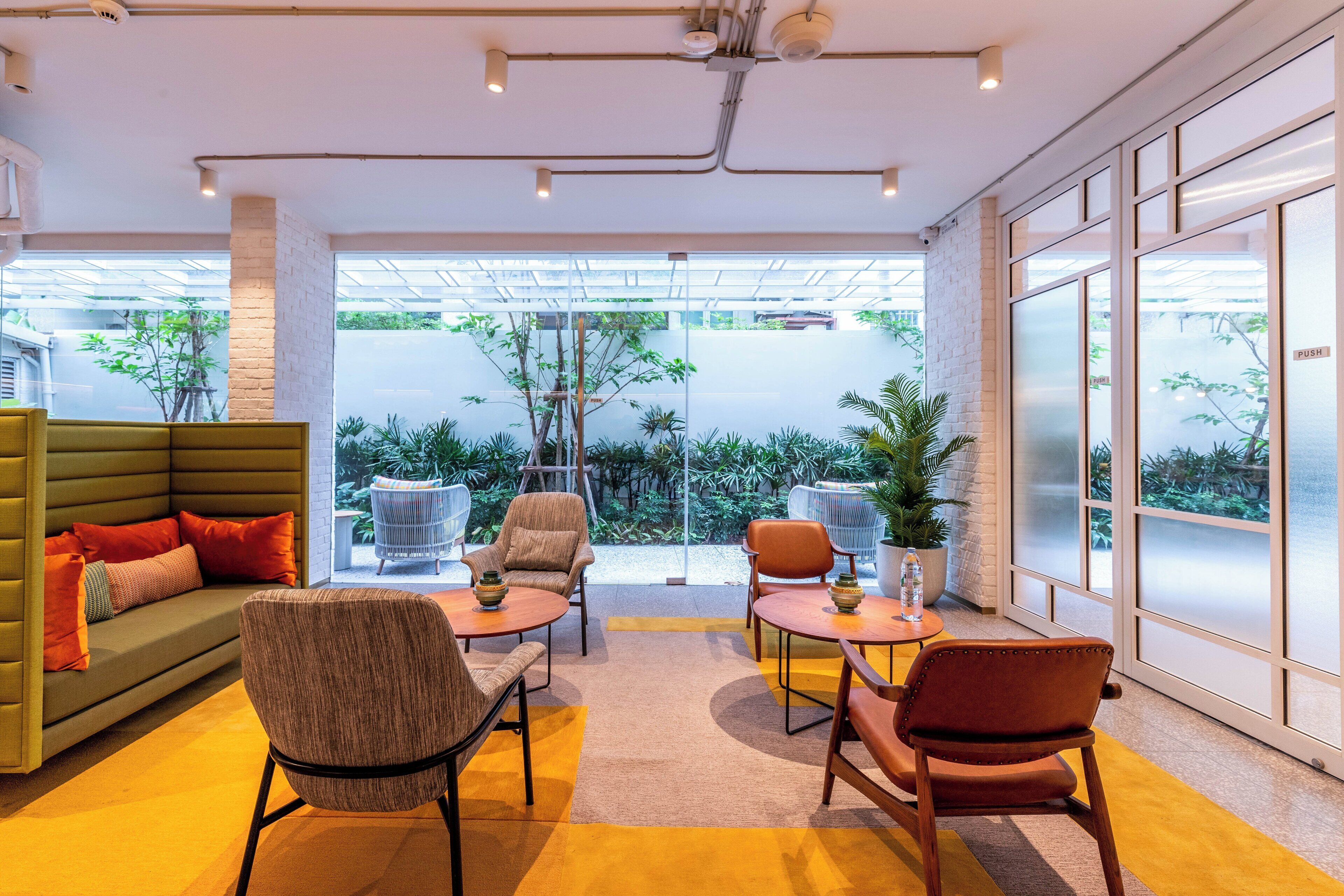Ein modernes Interieur mit einem grünen Sofa, zwei Sesseln und einem Couchtisch, eine Glastür zu einem Garten und ein großes Fenster mit Blick ins Grüne.