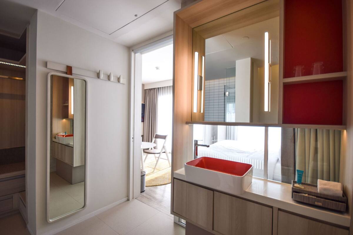 A modern bathroom with a large mirror, a red basin, and a view of a balcony.