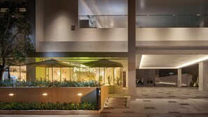 Een modern gebouw met een goed verlichte ingang, een zichtbaar restaurant genaamd 'Paradiso', en een bord met 'Shama Yen-Akat Bangkok'.