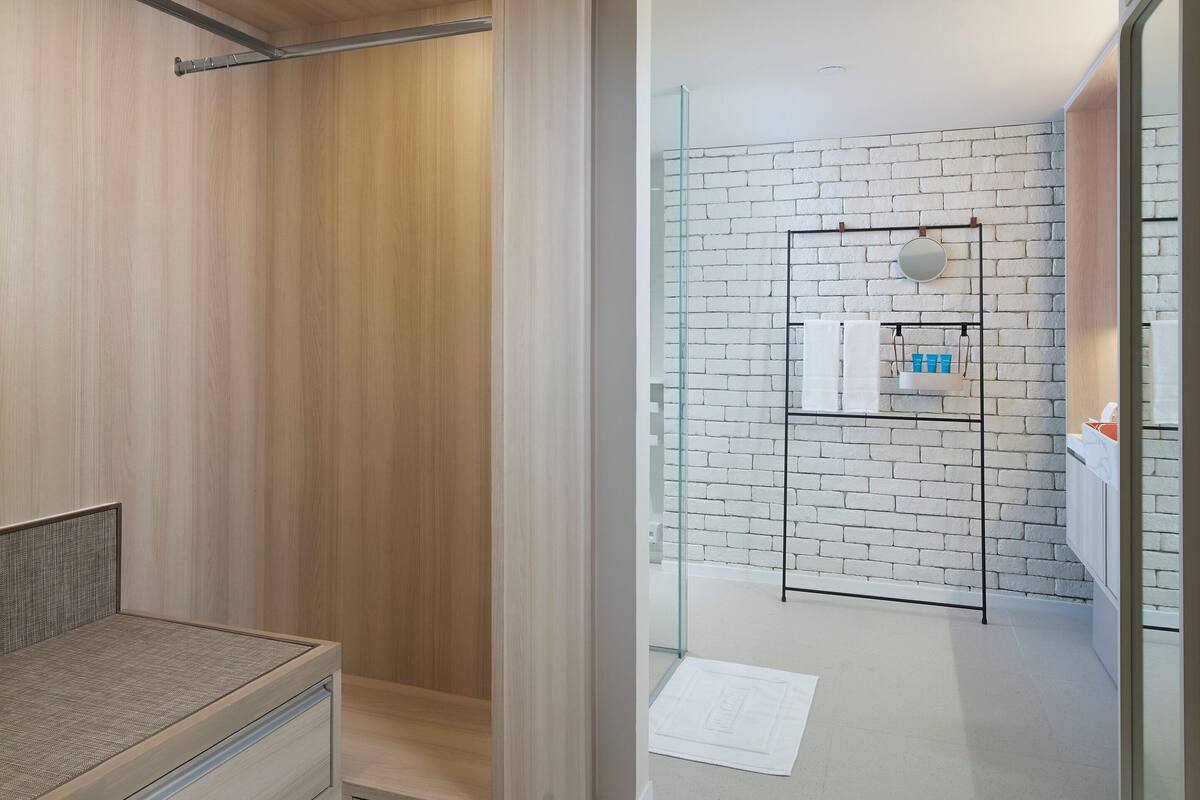 A modern bathroom with a wooden vanity, a glass shower enclosure, and a white brick wall.