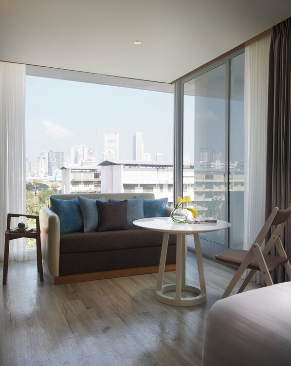 Quarto de hotel moderno com uma janela grande, um sofá, uma mesinha com um vaso e uma cadeira.