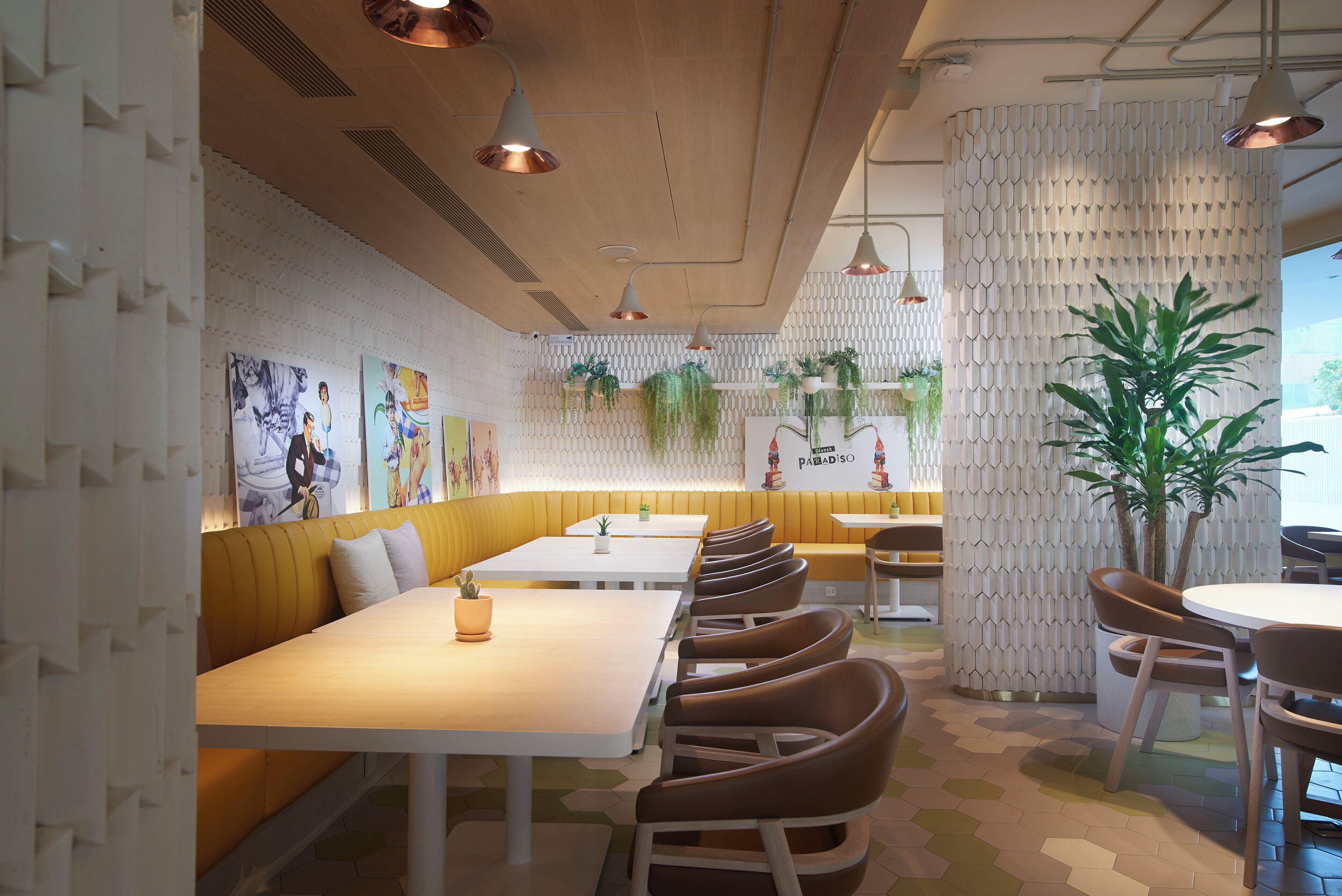 A restaurant interior with long tables, cushioned booths, hanging plants, and a patterned wall.