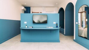 A reception area with a blue counter, a flat-screen TV, and a window with curtains. - Sorrento Colors&Suites (Sorrento)