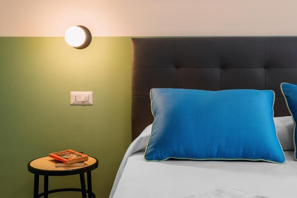 A room with a bed, a round table with a book, and a wall-mounted light.