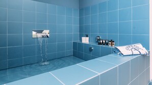 A bathroom with blue tiles, a bathtub, a showerhead, and toiletries on a shelf. - Sorrento Colors&Suites (Sorrento)