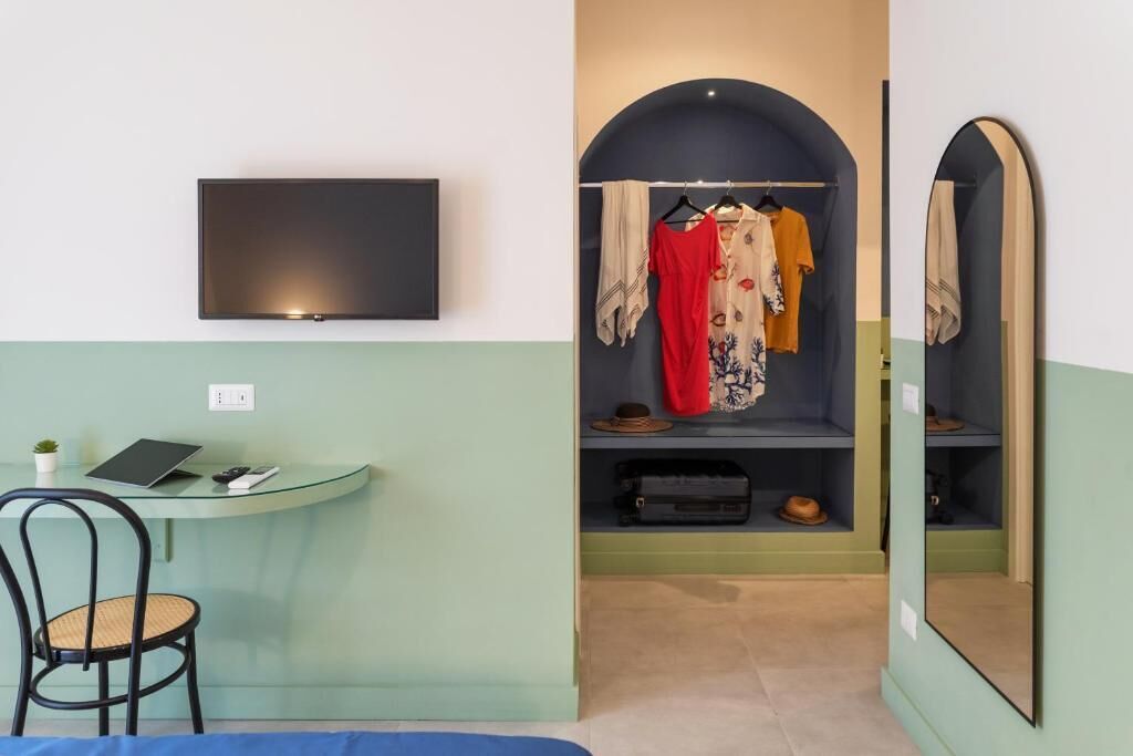 Een kamer met een bureau, stoel, televisie, kledingrek en spiegel.