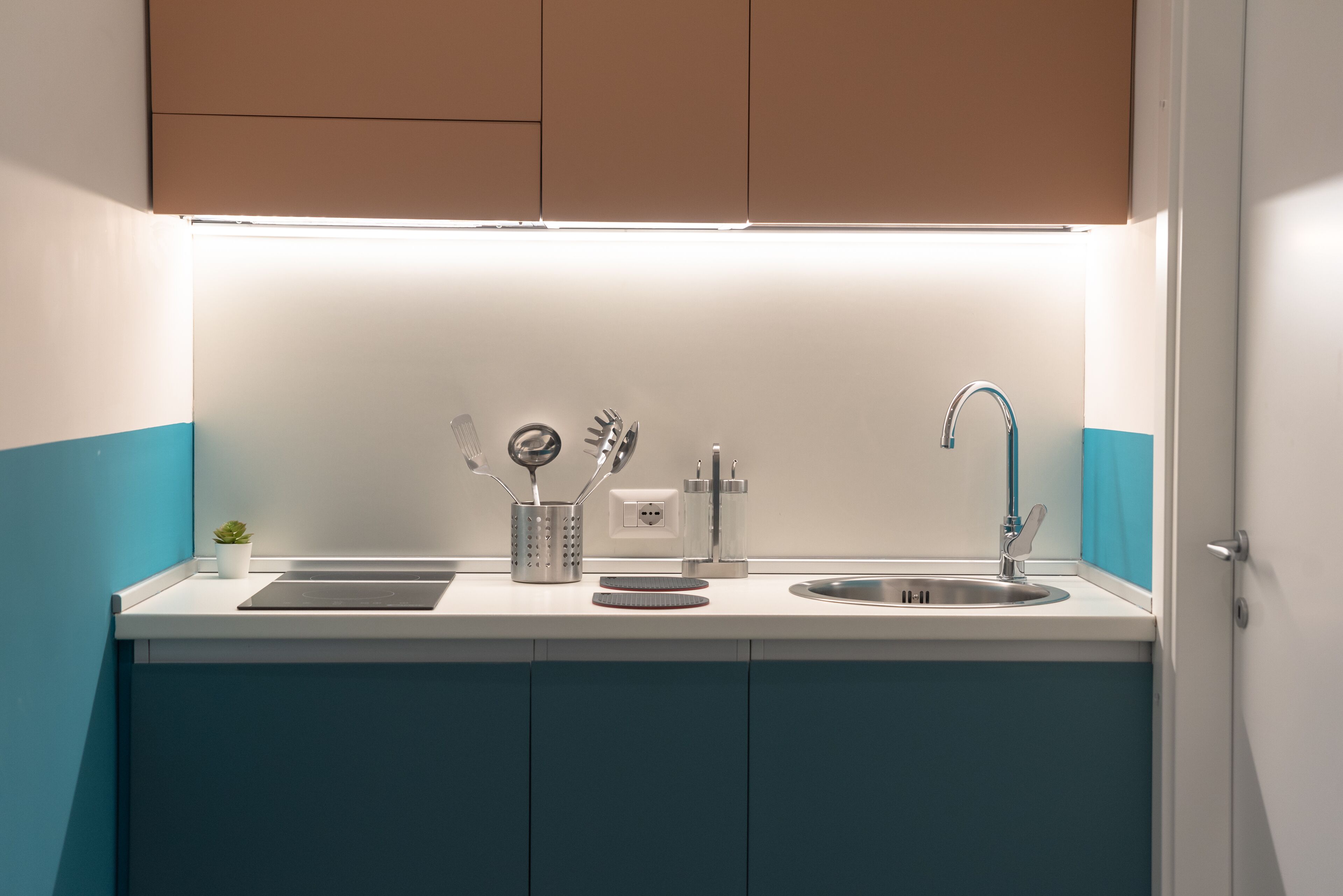 Una cocina moderna con encimera blanca, pileta de acero inoxidable y armarios azules.