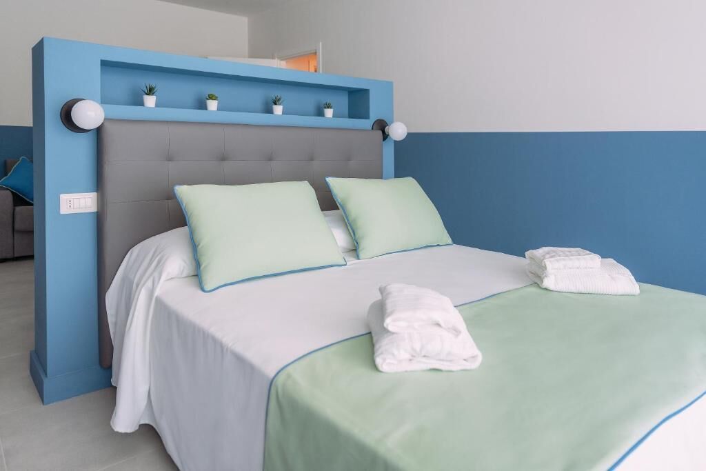 Un lit bien fait, avec une tête de lit grise, deux oreillers vert clair et une couverture blanche.