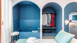 A room with a bed, a seating area, a clothing rack, and a shower area. - Sorrento Colors&Suites (Sorrento)