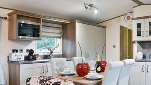 A modern RV kitchen with a dining area, white cabinetry, and a mounted television. - Boutique Lodge With hot tub Sleeps 6 (Bridlington)